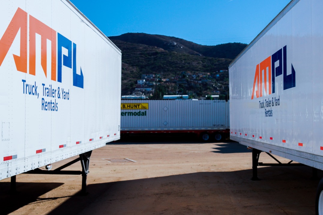 Two AMPL semi trucks parked next to each other in a lot